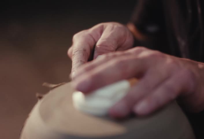 A skilled artisan carves and trims the base of a clay pot on a spinning pottery wheel in a workshop, captured in slow motion
