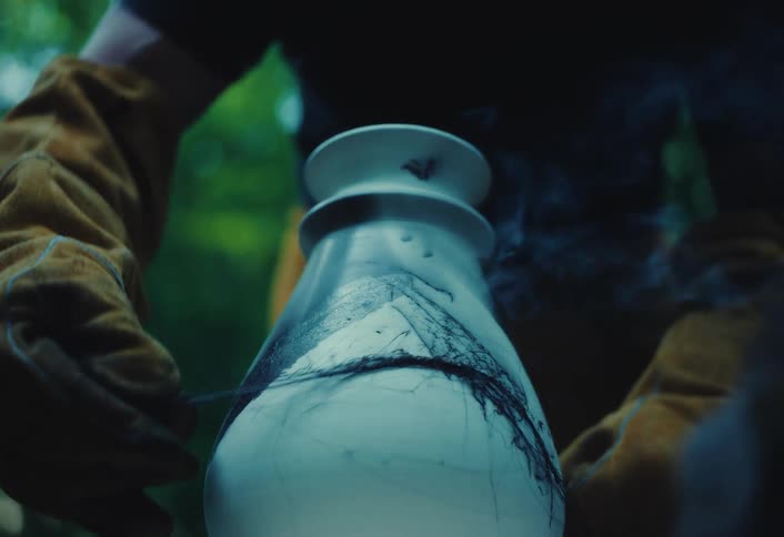 An artist carefully burns horsehair onto a hot pottery vase, creating intricate black lines and smoke