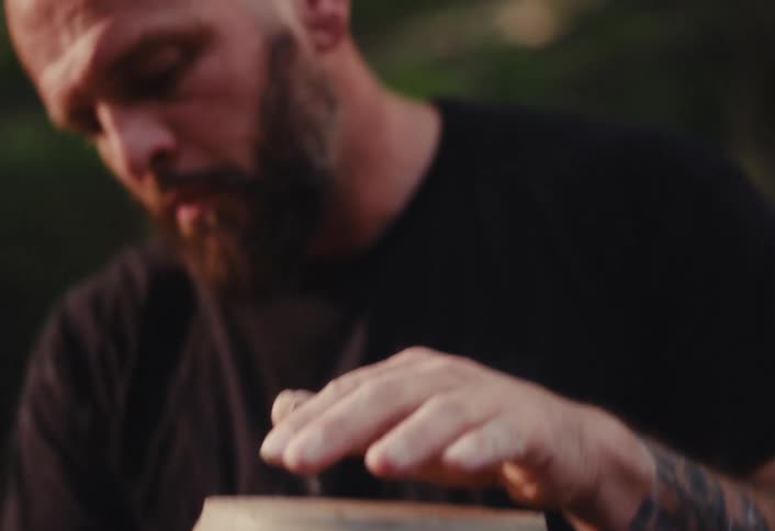 A skilled male potter with a beard and tattoos meticulously shapes a clay vase on a spinning pottery wheel