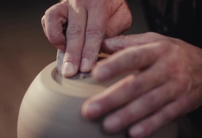 A potter carefully trims and shapes the base of a clay bowl on a spinning pottery wheel