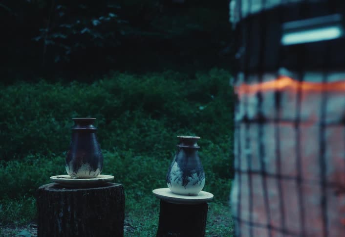 A pottery kiln glows orange with intense heat during the firing process as finished vases sit on display in the background at dusk