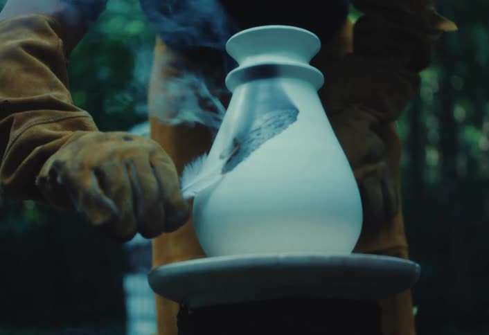 A potter carefully burns a feather onto a hot ceramic vase, creating a unique, smoky pattern on the surface