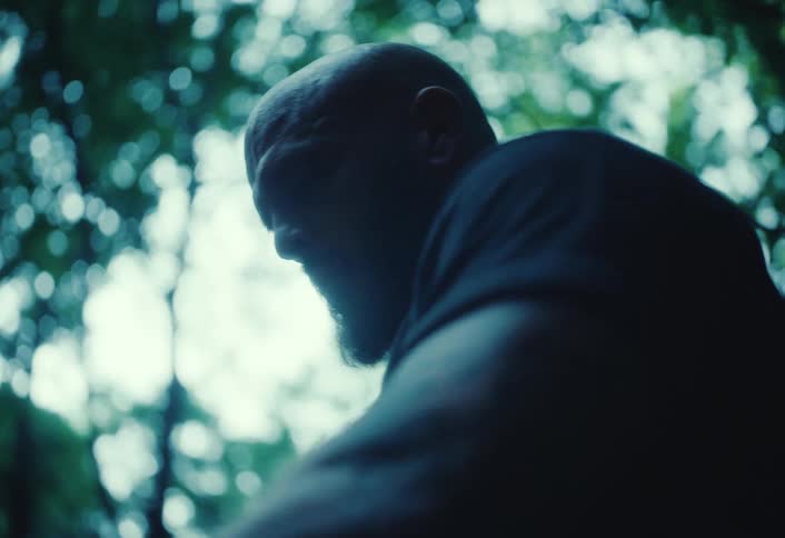 In slow motion, a man's hands put on a rugged work glove with a silhouetted figure in the moody forest background