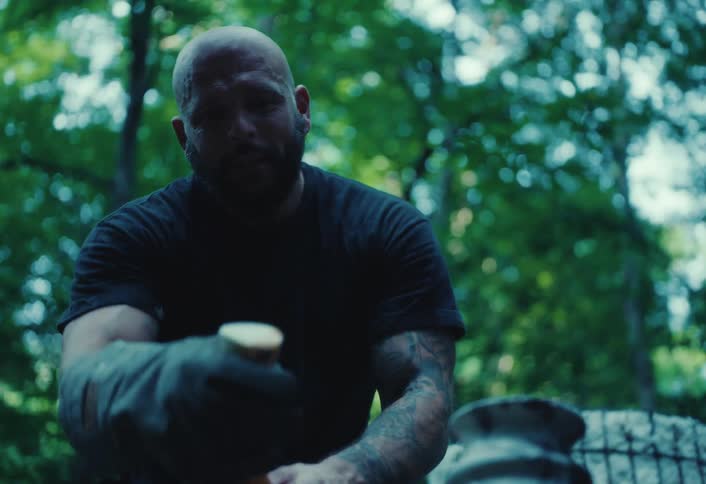 A potter with protective gloves carefully cleans and polishes a unique, marbled raku-fired vase in a wooded outdoor setting