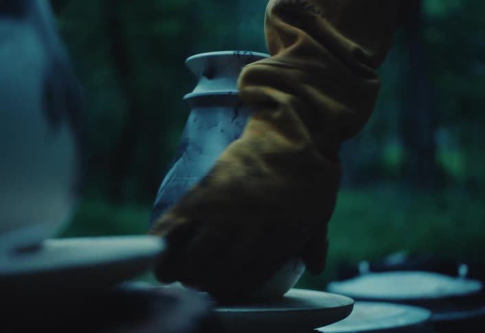 A potter's gloved hand gently touches a newly raku-fired vase as it steams and cools outdoors