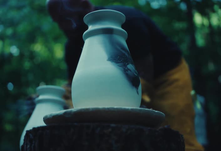 A potter wearing protective gloves carefully applies a feather to a hot ceramic vase, causing it to burn and create a unique smoky design