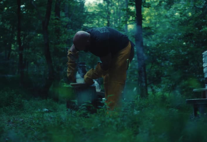 An artisan carefully works on a hot, smoking ceramic pot outdoors in a tranquil woodland setting
