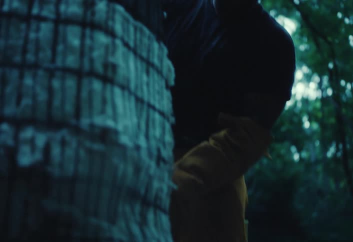 A serious craftsman wearing protective gear prepares his handmade kiln in a dark forest