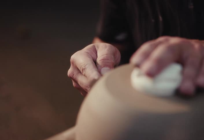 An artisan carefully trims and shapes a clay pot on a pottery wheel in slow motion