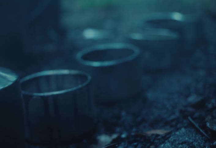 A mysterious out-of-focus shot of steaming metal mugs sitting on the dark ground