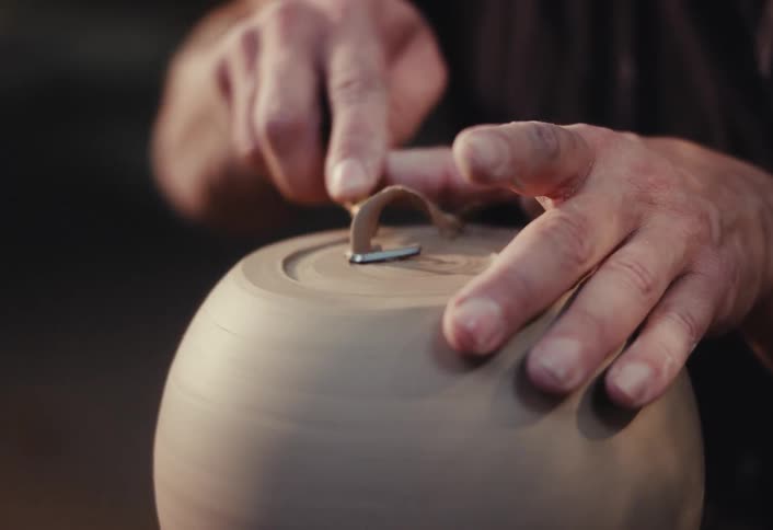 A skilled potter uses a trimming tool to carefully carve the foot of a leather-hard clay bowl spinning on a pottery wheel