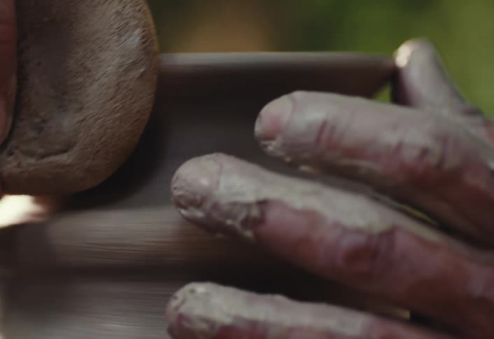 A potter's clay-covered hands meticulously shape a spinning piece of pottery on a wheel