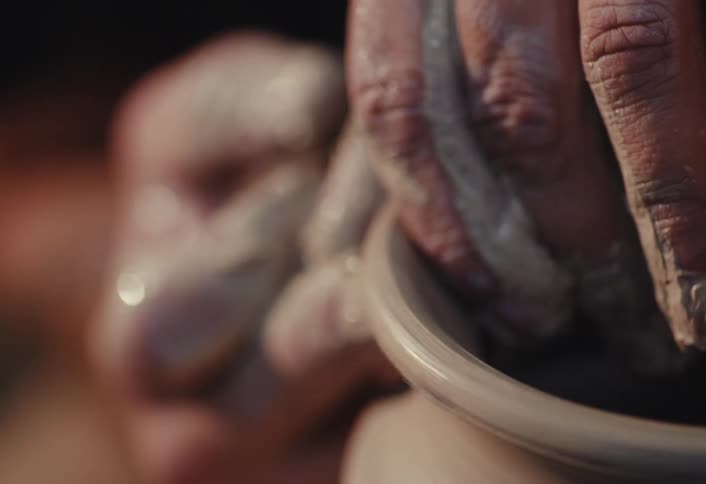 An artisan's hands meticulously shape a vase from wet clay on a spinning potter's wheel in a close-up slow-motion shot