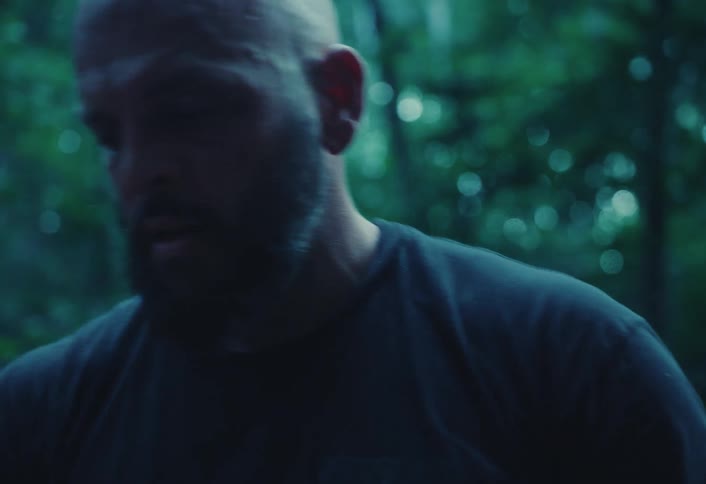 Slow motion close-up of a sweaty and determined man with a beard inspecting an axe in a moody forest