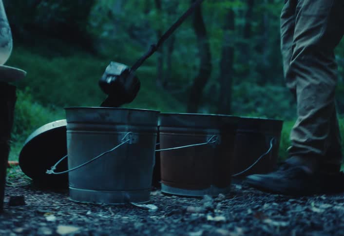 A crafter uses long tongs to remove a hot, smoking piece of Raku pottery from a bucket and place it on the ground to cool