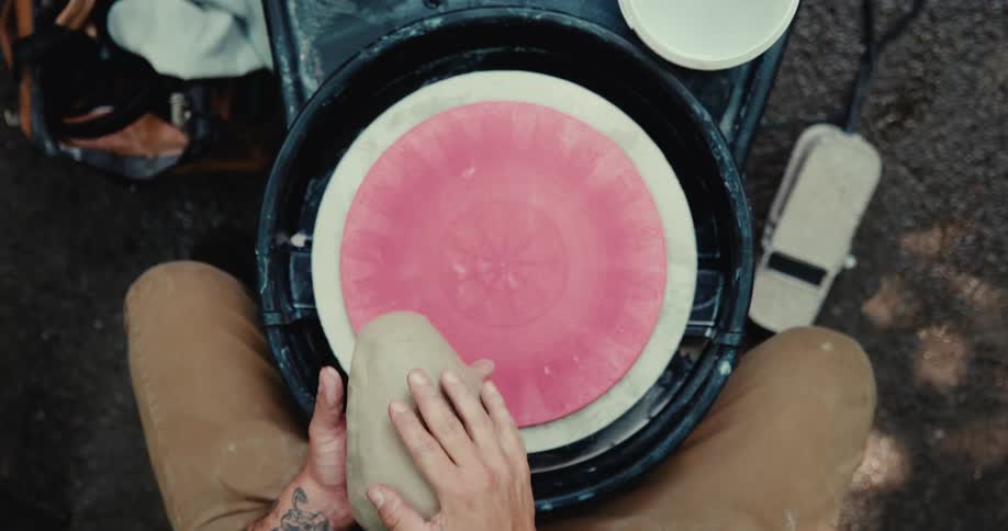 Top-down slow motion view of a potter with tattooed arms kneading clay and centering it on the wheel