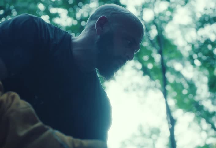 A mysterious low-angle shot reveals a bearded craftsman carefully working with his handmade pottery on a tree stump in the forest