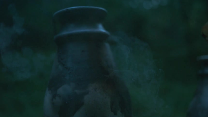 Close-up slow motion shot of a hand spraying a ceramic pot, causing an ethereal smoky mist to rise in the dusky light