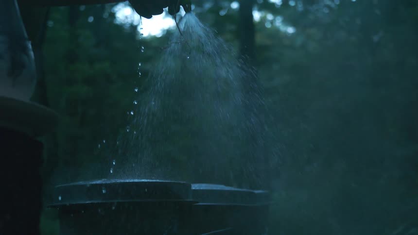 A gloved hand sprays steaming buckets with a water hose in a dark, misty forest in slow motion