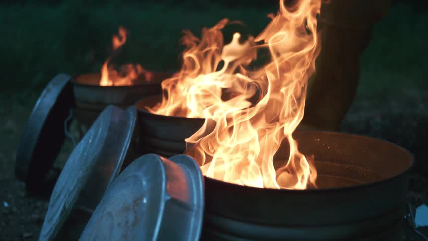 Flames dance in slow motion inside three metal trash cans burning brightly at night