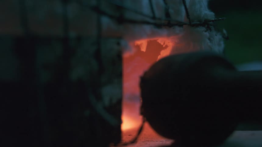 A small homemade propane forge roars with intense orange and blue flames in a dark workshop