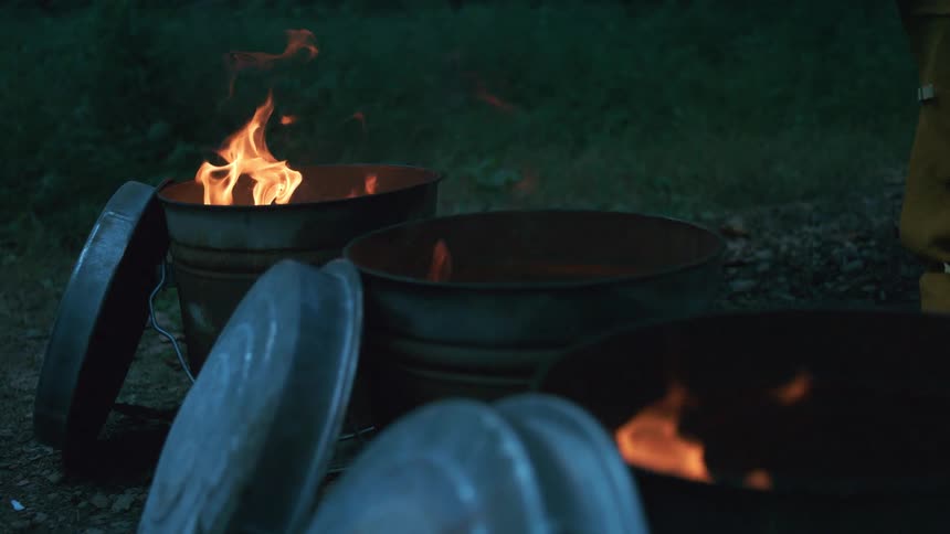 Slow motion shot of flames burning inside several rusty metal trash cans outdoors at night