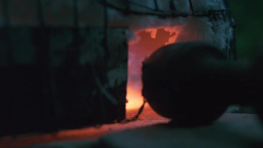 Flames and smoke billow from the opening of a hot kiln during the pottery firing process
