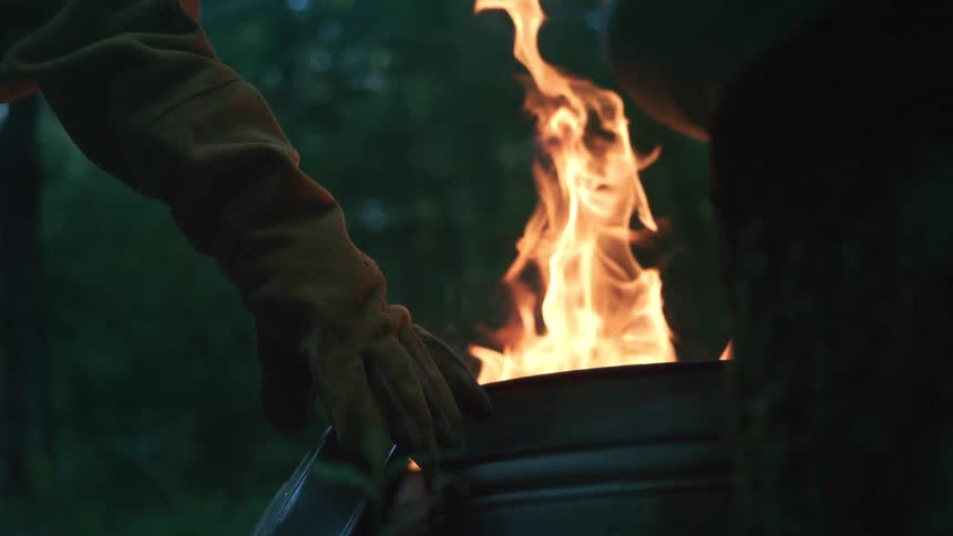 A mesmerizing slow motion close-up of a vibrant fire burning inside a barrel in the woods at dusk