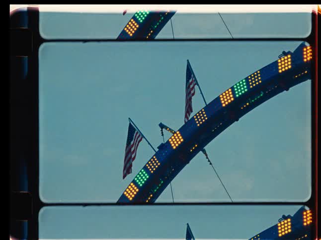 A low-angle shot of a carnival ride with flashing lights and American flags, captured on vintage film