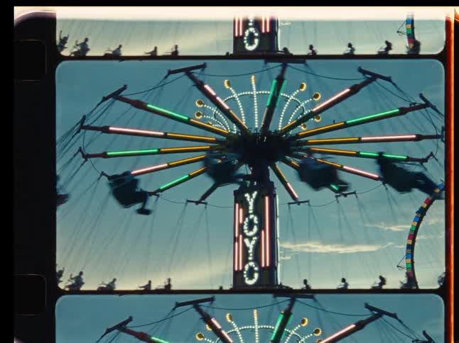 Silhouettes spin on a brightly lit 'Yo-Yo' swing ride at an amusement park in this retro, film-strip styled shot