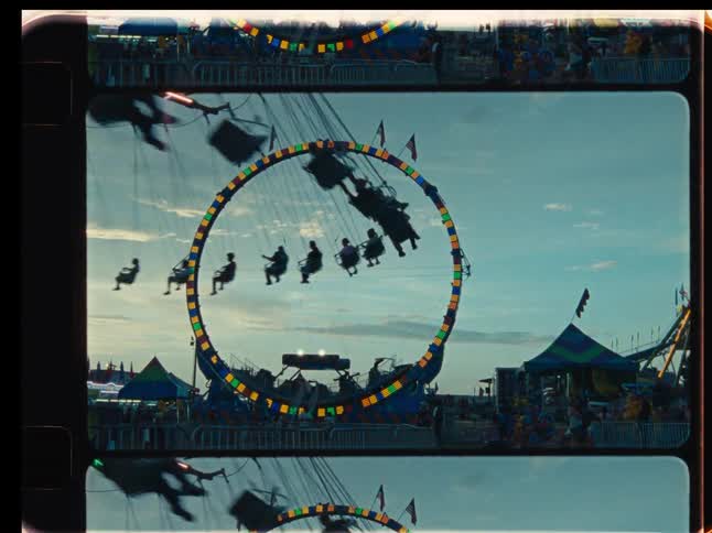 A nostalgic, vintage-style film clip shows silhouetted people enjoying a spinning swing ride at a carnival against the evening sky