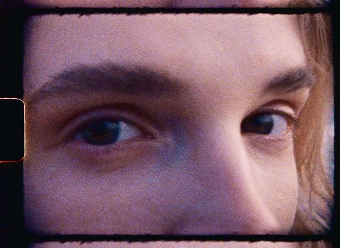 An extreme close-up shot of a person's eyes, captured on grainy, vintage-style film with a visible frame