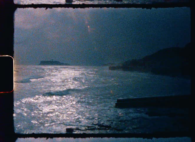 Vintage 8mm film captures the shimmering San Francisco Bay with Alcatraz Island in the distance, followed by a shot of surfers riding waves