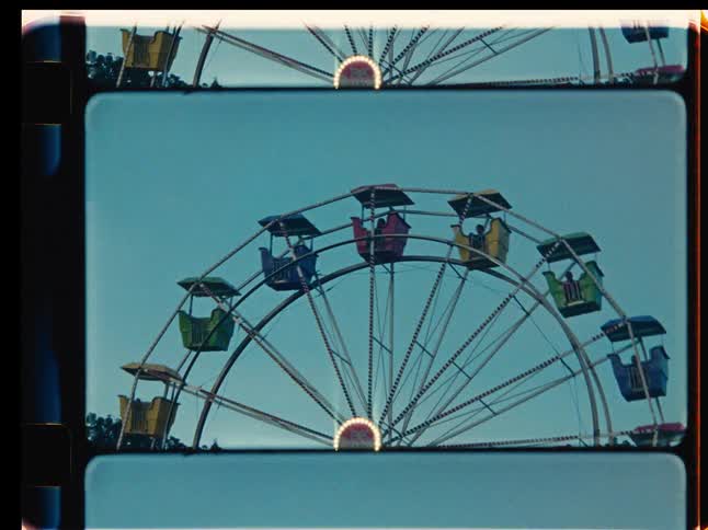 Vintage 8mm film-style footage of a brightly lit Ferris wheel spinning at a fair during dusk