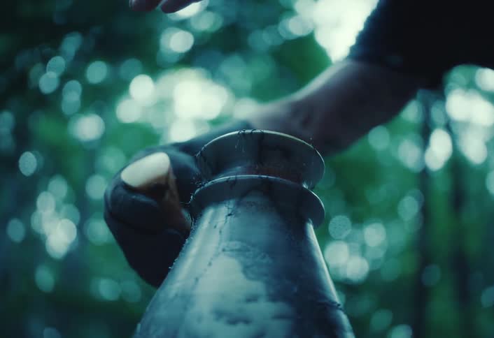 Slow motion close up of a gloved hand pouring liquid onto a hot, steaming ceramic vase as part of a mysterious craft in a moody forest