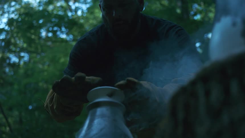 Slow motion shot of a bearded artisan carefully handling a smoking hot ceramic vase outdoors in a dark forest