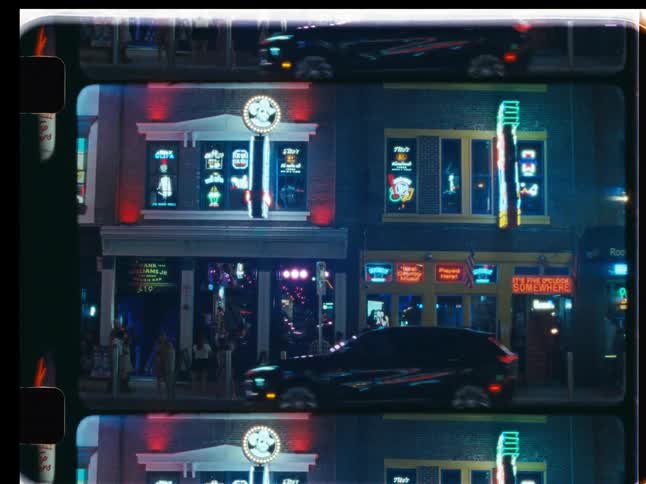 A vintage film view of a bustling city street at night, illuminated by the vibrant glow of neon signs from local bars