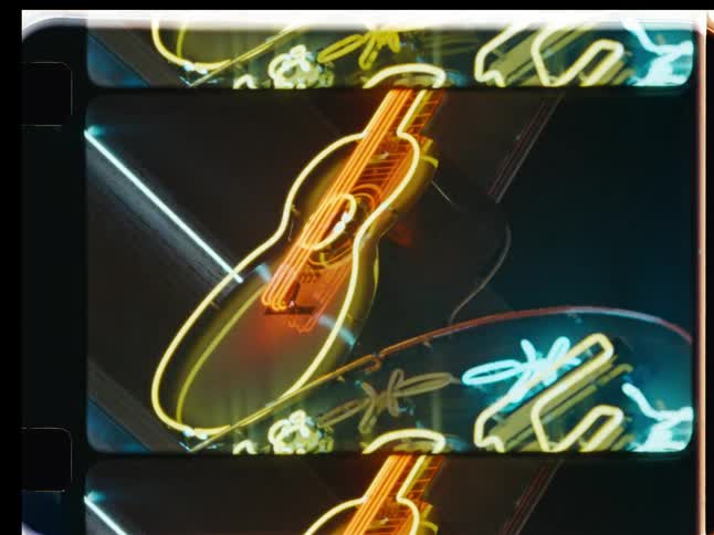 Vintage film strip effect on a close-up of a flickering neon guitar and cowboy hat sign at night