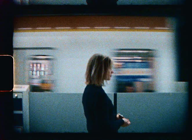 A nostalgic film shot of a young woman standing on a subway platform as a train speeds by in the background