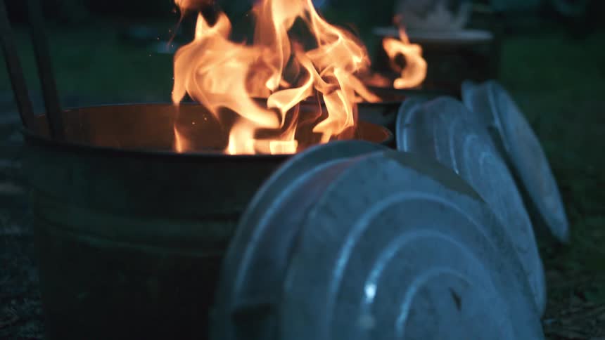 Slow-motion flames flicker and dance inside metal burn barrels with their lids off to the side