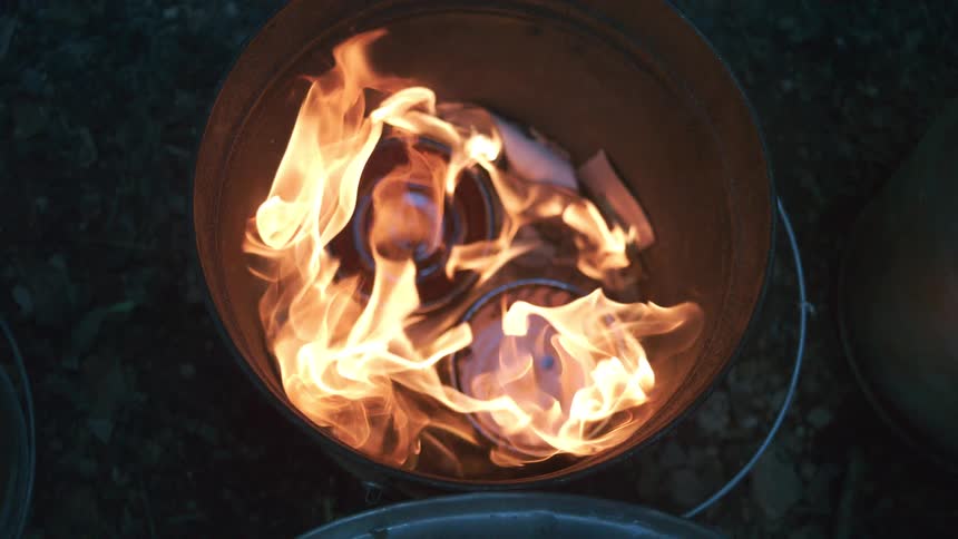 A mesmerizing top-down slow-motion shot of a fire burning inside a metal bucket at night