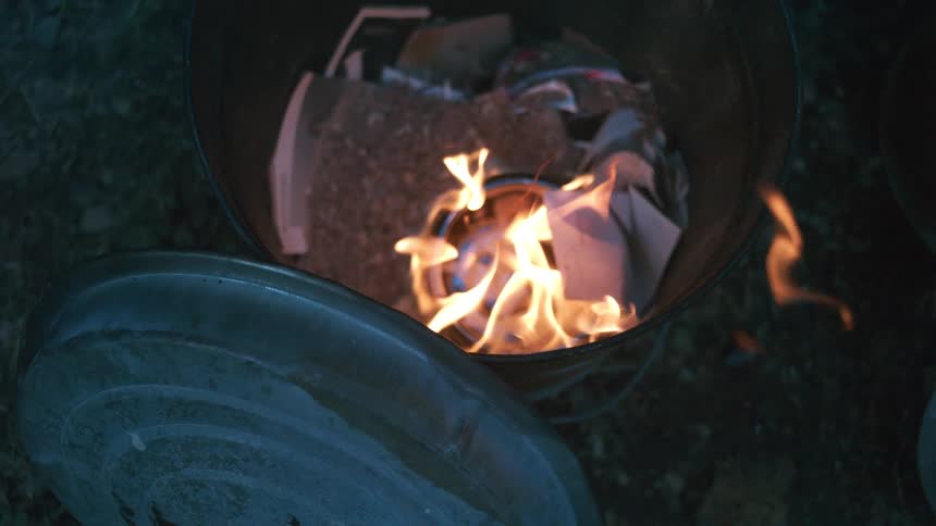Close-up slow motion of a fire burning inside a garbage can at night