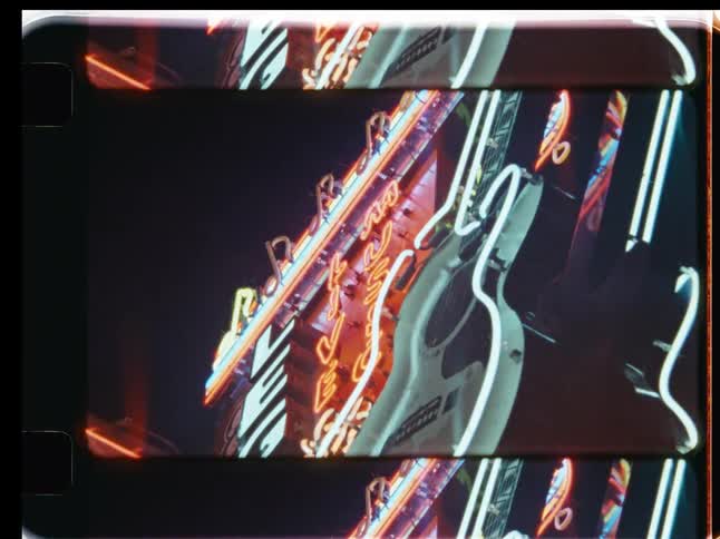 A distorted, flashing Rock and Roll neon guitar sign glows brightly at night in this vintage film-style clip