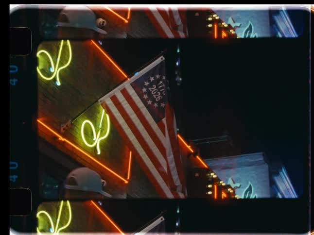 Vintage film shot of a USA Semiquincentennial flag illuminated by neon signs on a city street at night