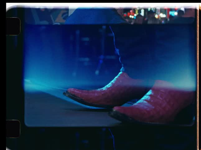 A stylized, vintage film aesthetic shows a man in a cowboy hat on a neon-lit street and a musician's boots on stage