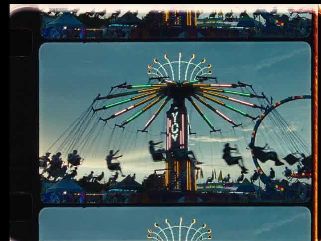 Silhouettes of people on a spinning Yo-Yo swing ride at a carnival during sunset, captured on vintage-style film