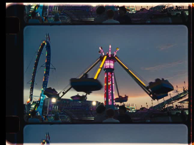 A spinning carnival ride glows with colorful lights against the sunset, captured in a nostalgic vintage film style