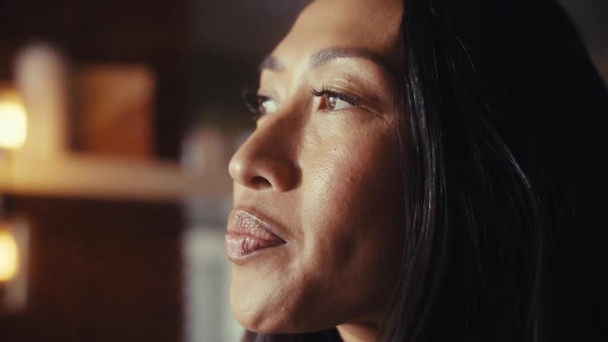 Close-up profile of a pensive woman's face as her expression softens into a gentle, hopeful smile