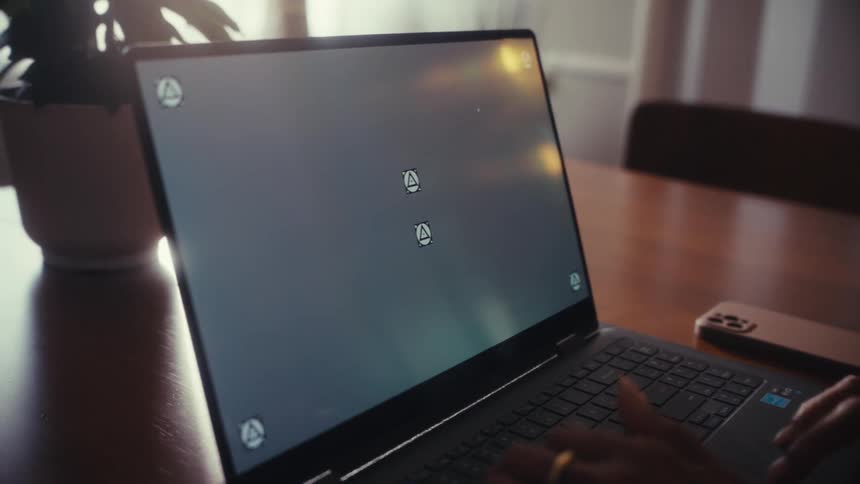 Close-up of a person's hands typing on a laptop with a tracking screen, set on a sunlit table next to a smartphone