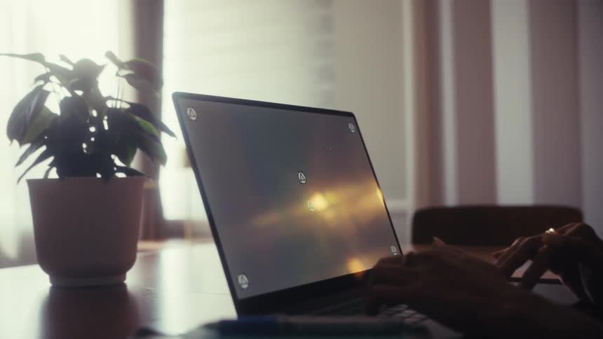 A person's hands are shown typing on a laptop with tracking markers on the screen in a sun-drenched home office